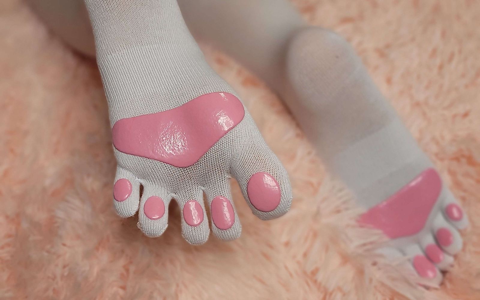 A pair of cream Cherry Frost socks with glossy pink toe beans, resting on a peach fluffy blanket